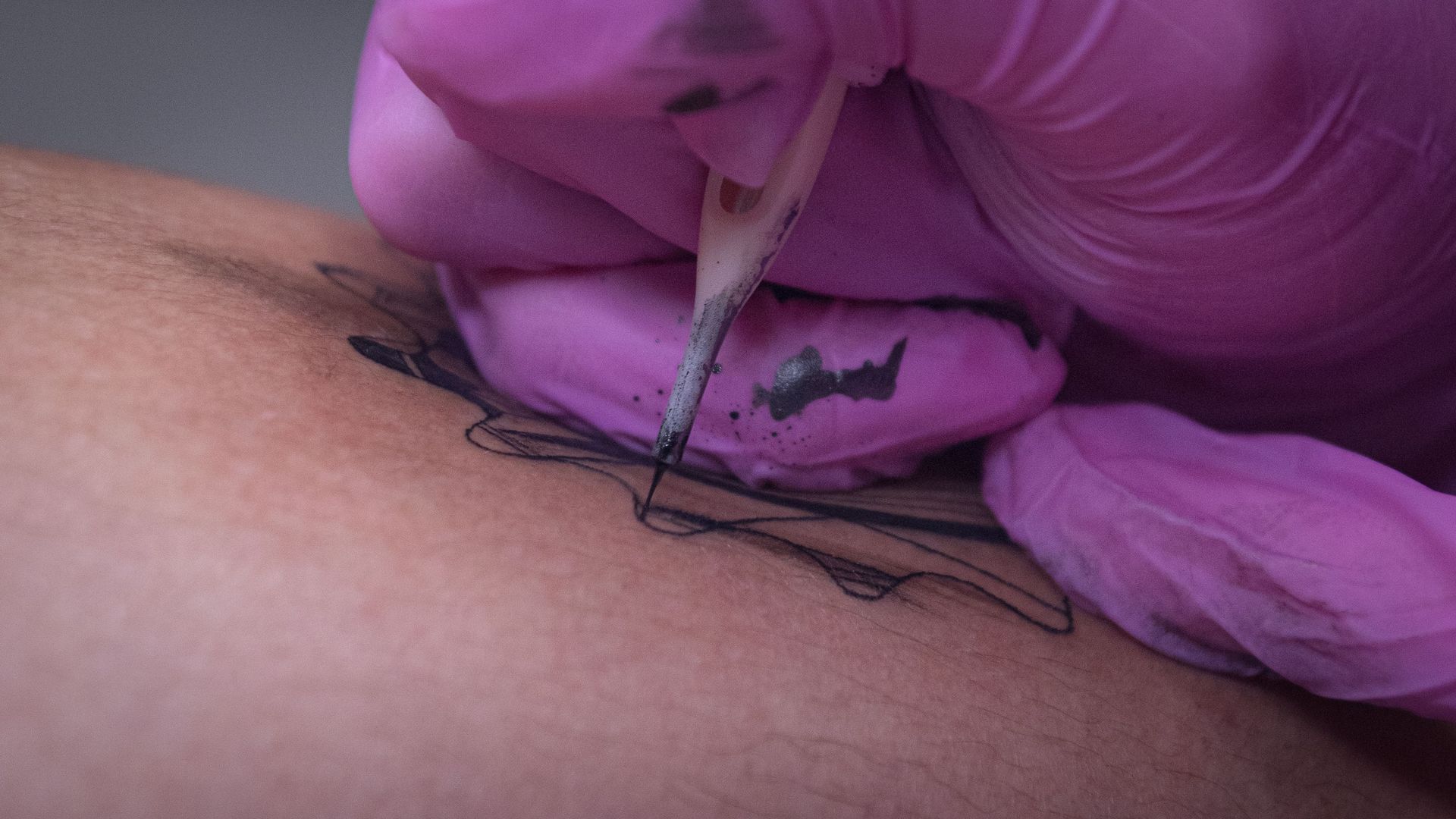Close-up view of a tattoo artist inking a design on human skin.