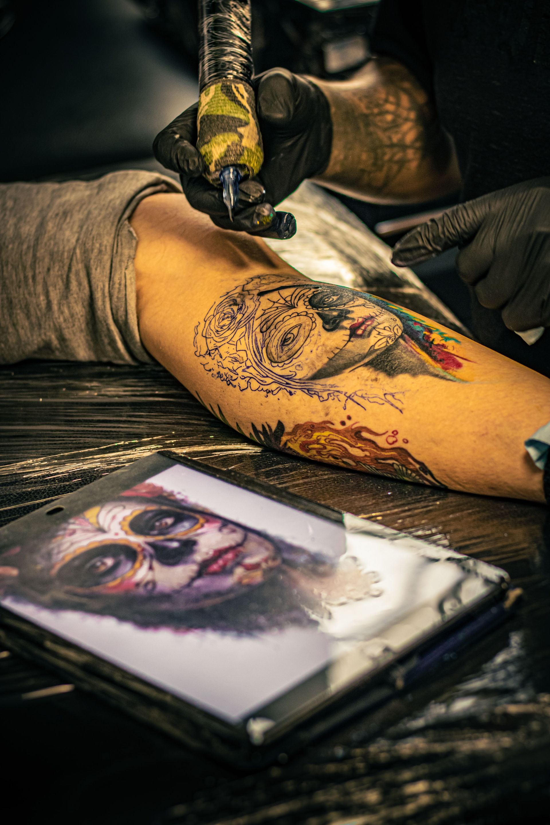 Tattoo artist creates intricate Day of the Dead design on a client's arm.