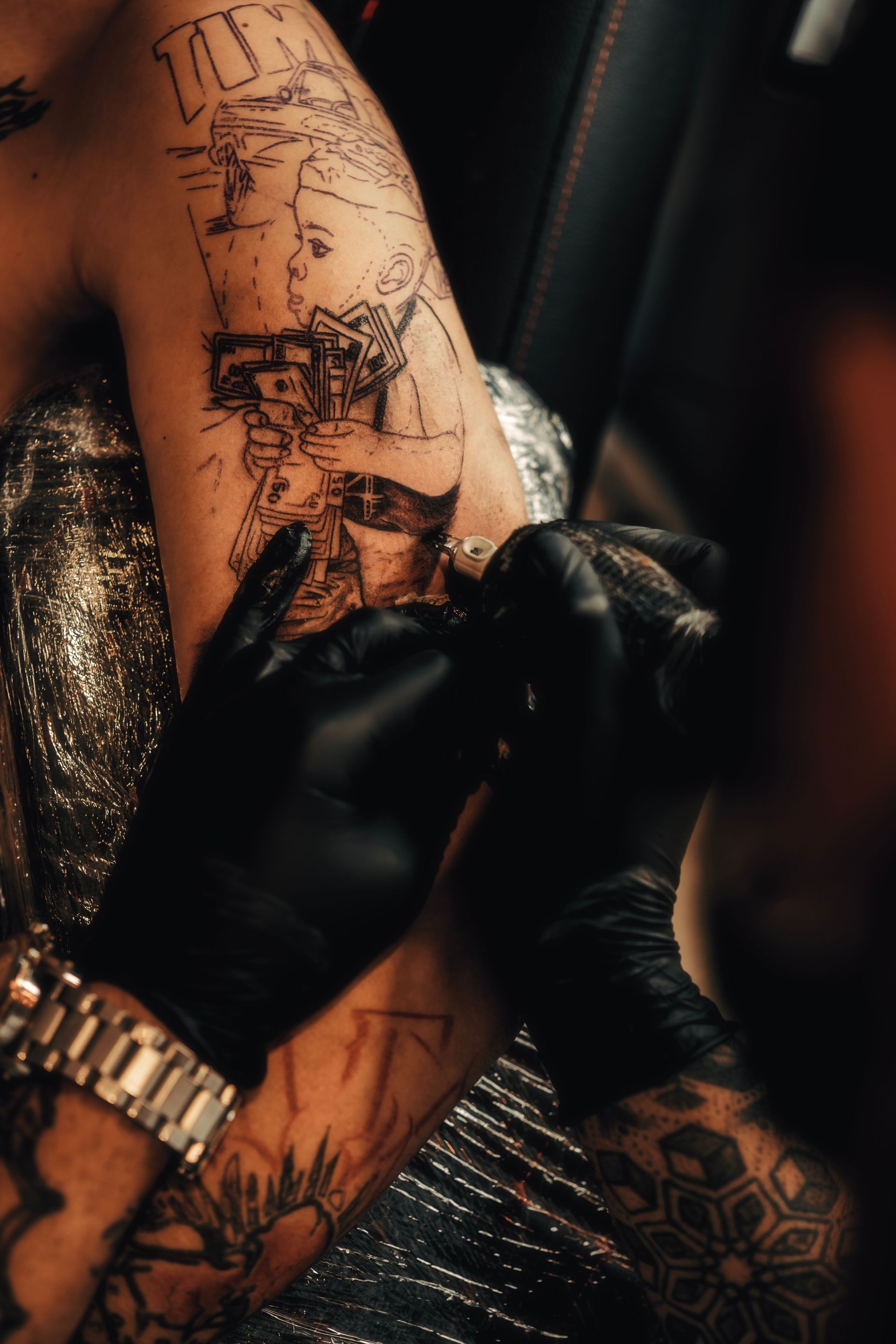 Close-up shot of an artist tattooing a detailed design on an arm with gloves.